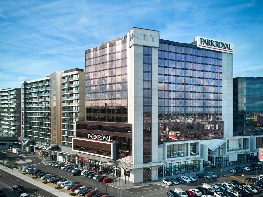 A multi-story hotel with a prominent 'PARKROYAL' sign, a parking lot, and a 'M-CITY' sign on the building.