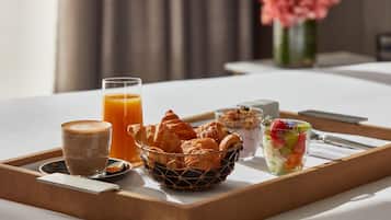 En bricka med frukost: croissanter, ett glas apelsinjuice, en kopp kaffe, en skål med müsli och en fruktsallad, placerad på ett bord på hotellet.