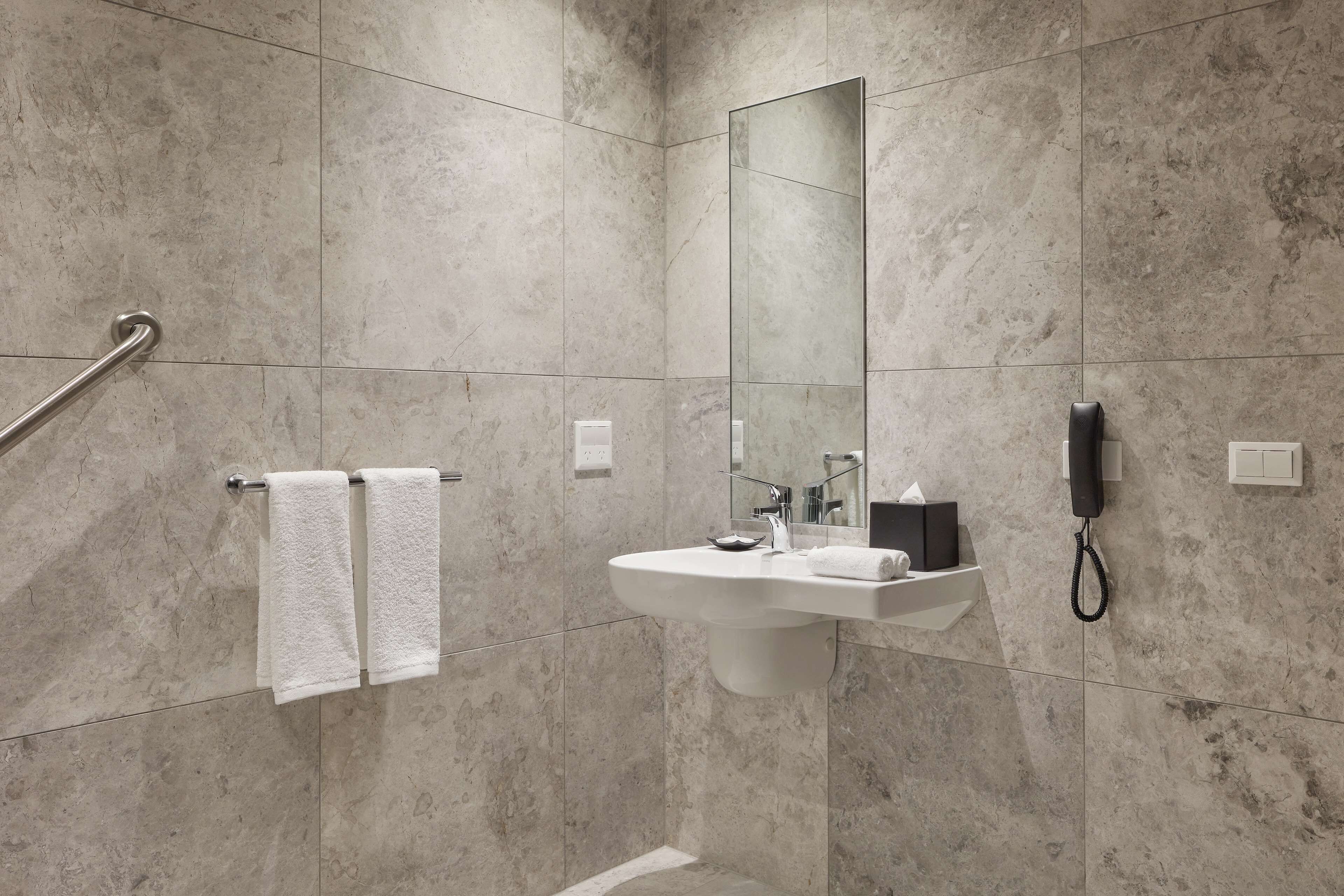 Un baño moderno con suelo de mármol, un lavabo blanco, un espejo, un perchero para toallas y un teléfono.