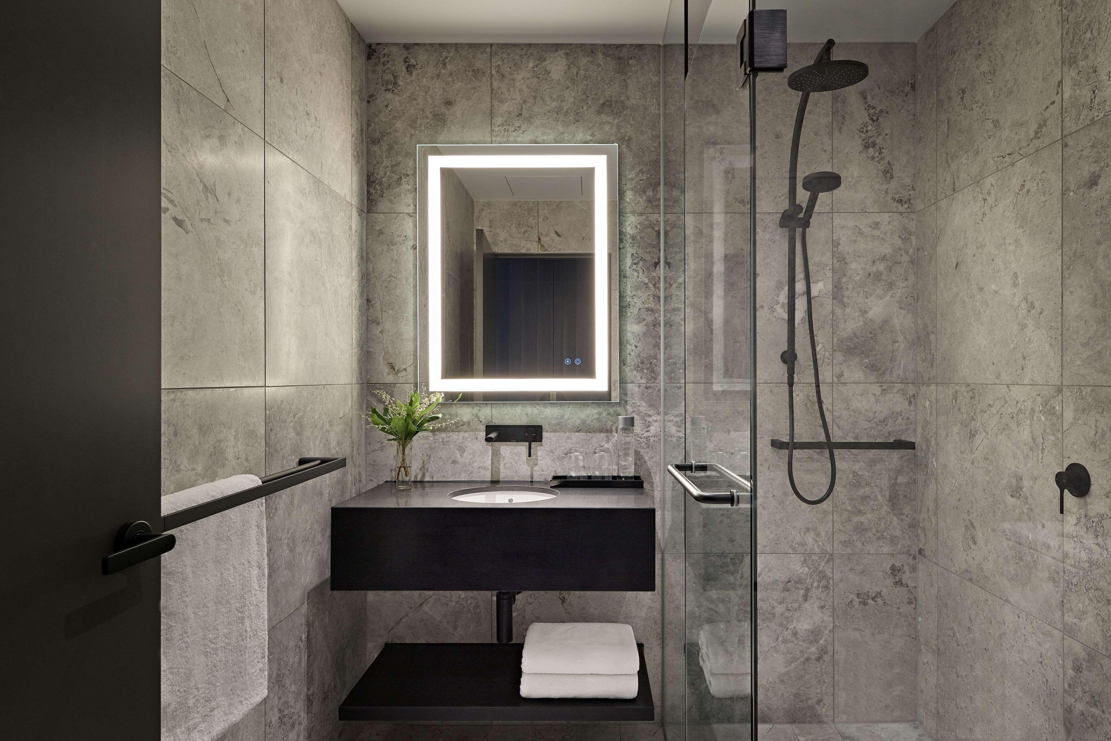 Un bagno moderno con un mobile lavabo scuro, uno specchio con illuminazione integrata e una zona doccia.