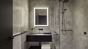 Un bagno moderno con un mobile lavabo scuro, uno specchio con illuminazione integrata e una zona doccia.