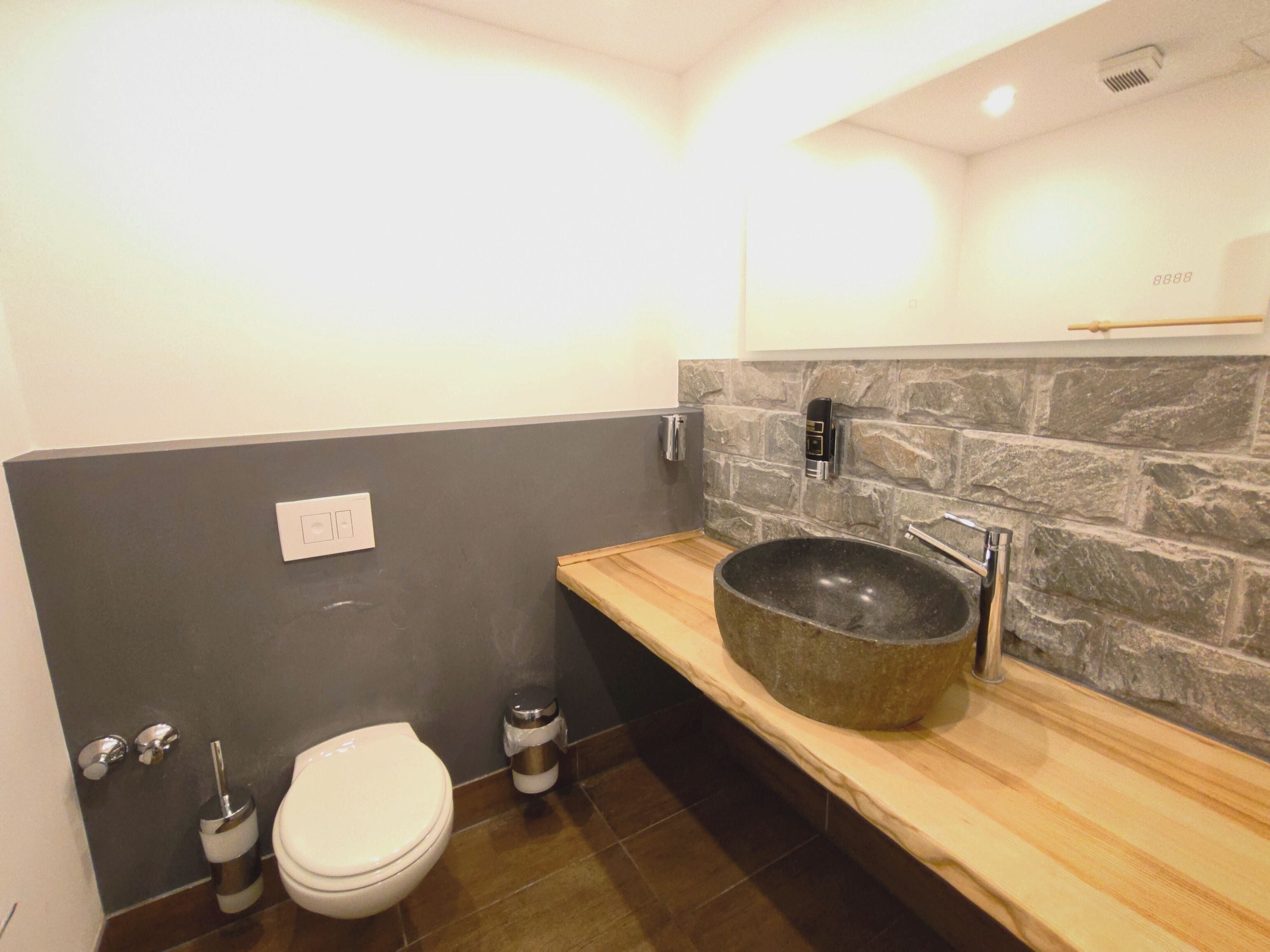 Un bagno moderno con una parete in pietra, un mobile lavabo in legno, un lavandino grande, un water e un bidet.