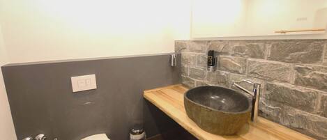 Un bagno moderno con una parete in pietra, un mobile lavabo in legno, un lavandino grande, un water e un bidet.