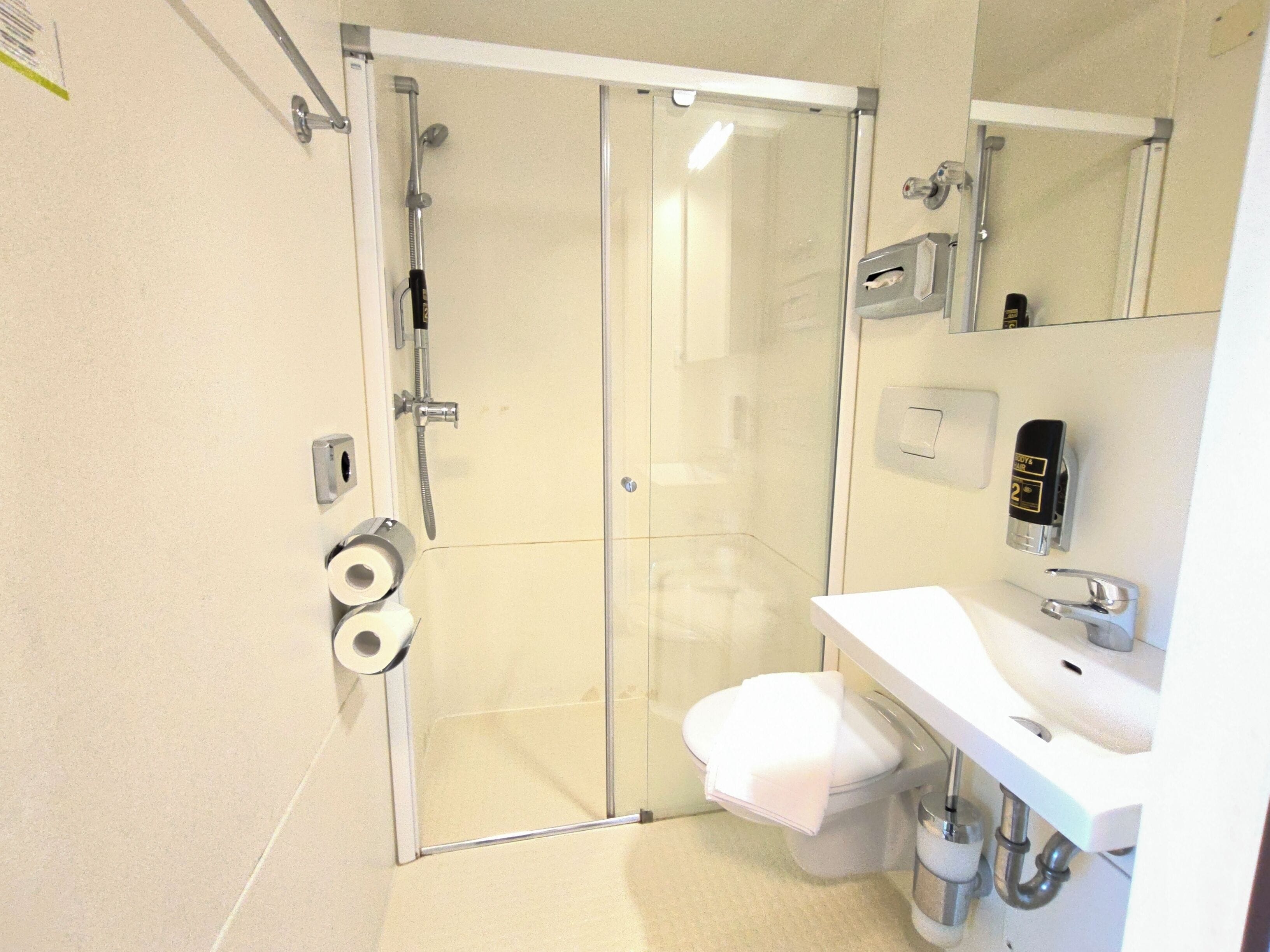 A bathroom with a glass shower enclosure, toilet, and sink.