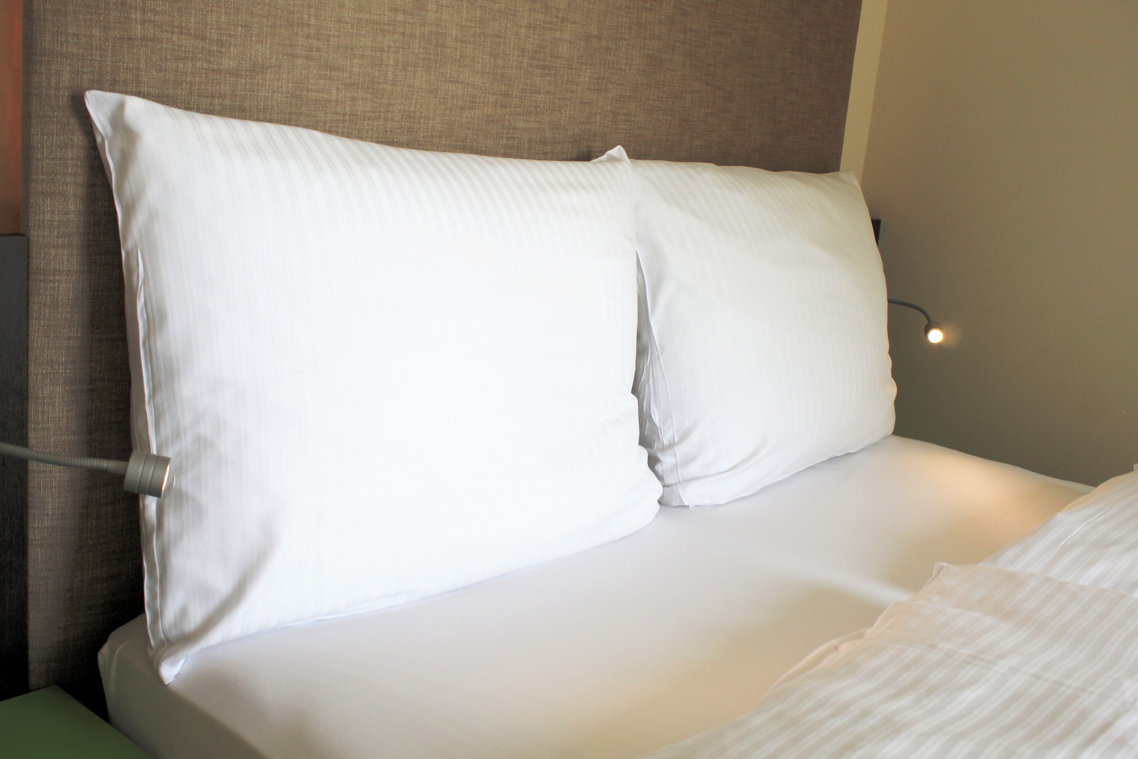 Un lit bien fait, avec du linge de lit blanc et des oreillers, une tête de lit et une lampe de chevet.
