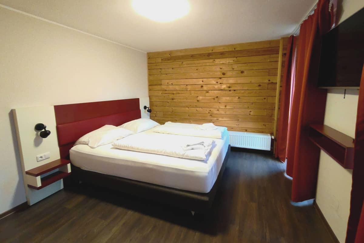 Ein Schlafzimmer mit Holzwand, einem Bett, einem Nachttisch, einer Lampe und einer Heizung.