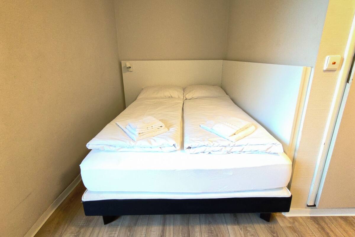 Ein Einzelbett mit weißer Bettwäsche und Handtüchern, ein Kopfteil und ein Holzboden.