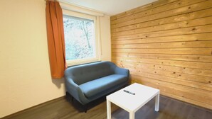A room with a wooden wall, a window with curtains, a blue sofa, and a white table. - Bendorf Hotel by Belvilla (Bendorf)