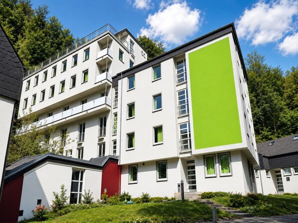 Ein mehrstöckiges Gebäude mit Balkonen, daneben ein rotes Gebäude und eine grüne Fassade.
