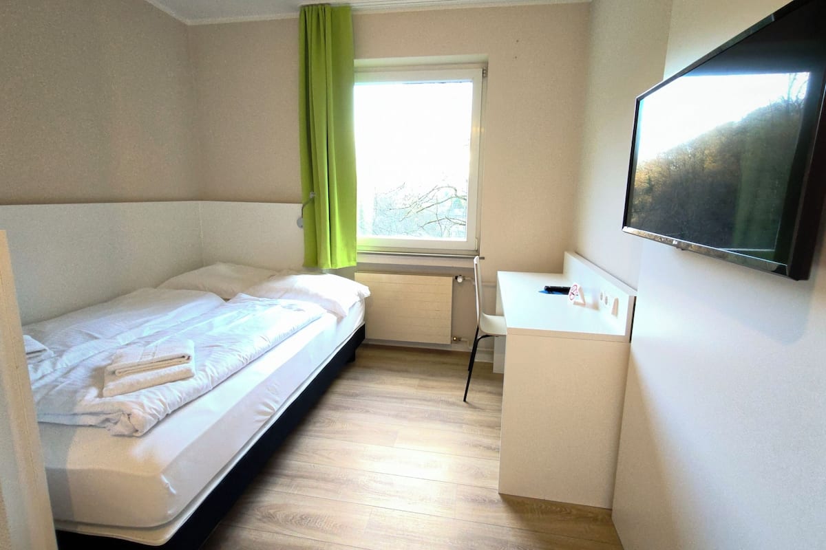 Ein Hotelzimmer mit einem Bett, einem Schreibtisch, einem Stuhl und einem an der Wand befestigten Fernseher.