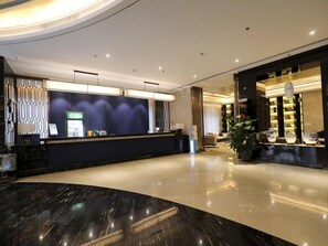 A hotel lobby with a reception desk, a seating area, and a display of decorative items. - Greentree Eastern Jingde Town Railway Station Hotel (Jingdezhen)