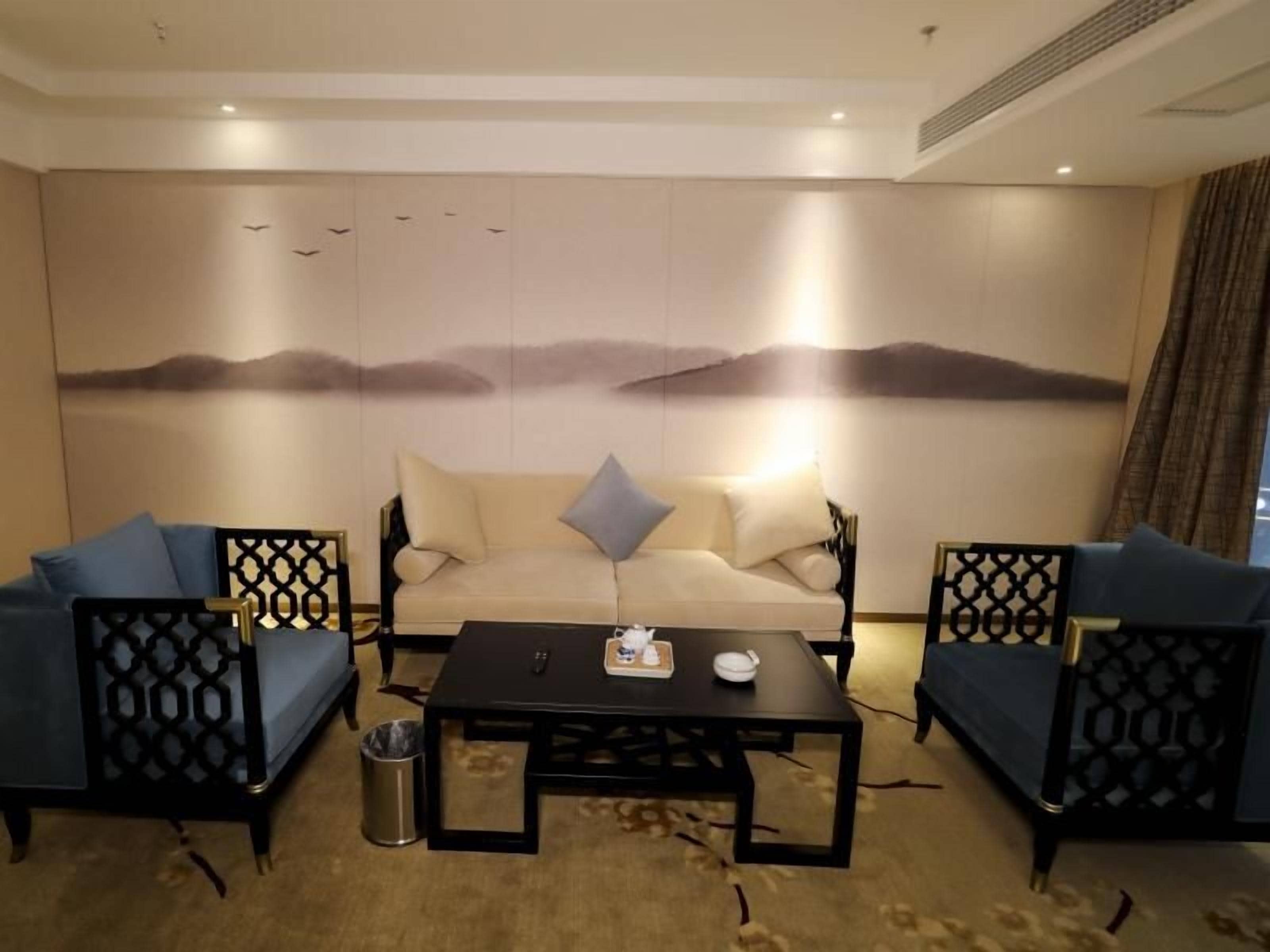 A room with a sofa set, a coffee table, and a decorative wall with a nature scene.