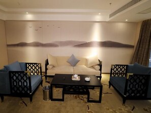 A room with a sofa set, a coffee table, and a decorative wall with a nature scene. - Greentree Eastern Jingde Town Railway Station Hotel (Jingdezhen)