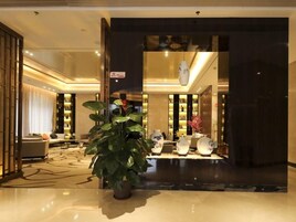 A hotel lobby with a large potted plant, a reception desk, and a seating area with a sofa and armchairs.