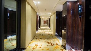 Pasillo de hotel con alfombra floral, puertas de madera y una cámara de seguridad en el techo.