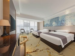 Habitación de hotel con dos camas, un escritorio, una silla, un televisor y un cuadro abstracto grande en la pared.