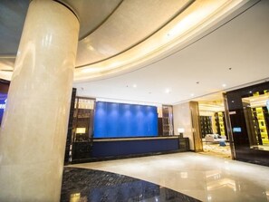 A modern lobby with a curved reception desk, a large pillar, and a blue accent wall. - Greentree Eastern Jingde Town Railway Station Hotel (Jingdezhen)