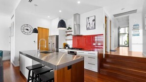 A modern kitchen with a central island, stainless steel appliances, and a red backsplash. - Sea Bliss (KINGSCLIFF)