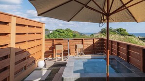 Una terraza de madera con un jacuzzi, dos sillas de mimbre y una sombrilla.
