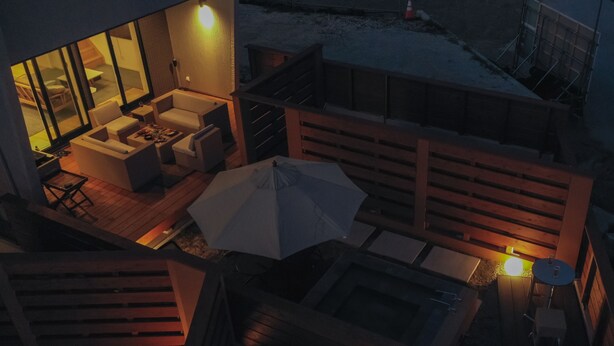 Un área al aire libre moderna con terraza de madera, mobiliario y una mesa bajo una sombrilla.