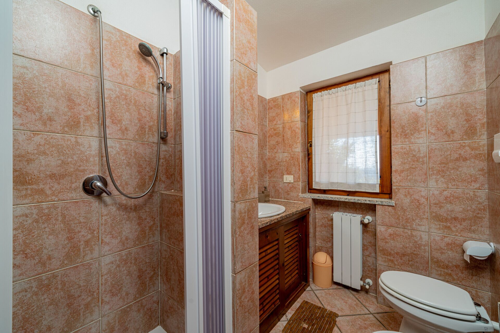 Een badkamer met douche, wastafel, toilet en een raam.