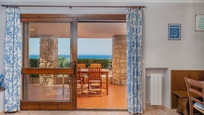 Une pièce dotée d’une porte-fenêtre coulissante donnant sur un patio extérieur avec un mur en pierre et une vue sur la mer.
