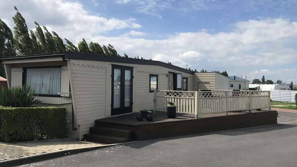 A mobile home with a front porch, a small deck, and a fenced area.