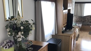 A modern living room with a wooden cabinet, a black ottoman, a TV, and a large mirror.