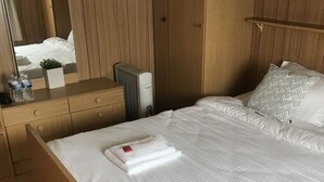 A hotel room with a wooden bed, a bedside table with a mirror, and a small potted plant.
