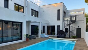 A modern house with a swimming pool, a wooden deck, and a spiral staircase.