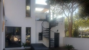 A modern building with a wooden deck, a spiral staircase, and a large tree.