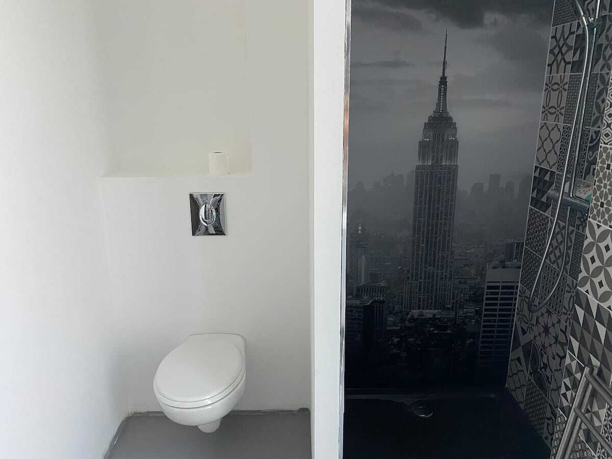 Une salle de bain équipée de toilettes, d’un miroir et offrant une vue sur le paysage urbain, notamment sur un gratte-ciel imposant.