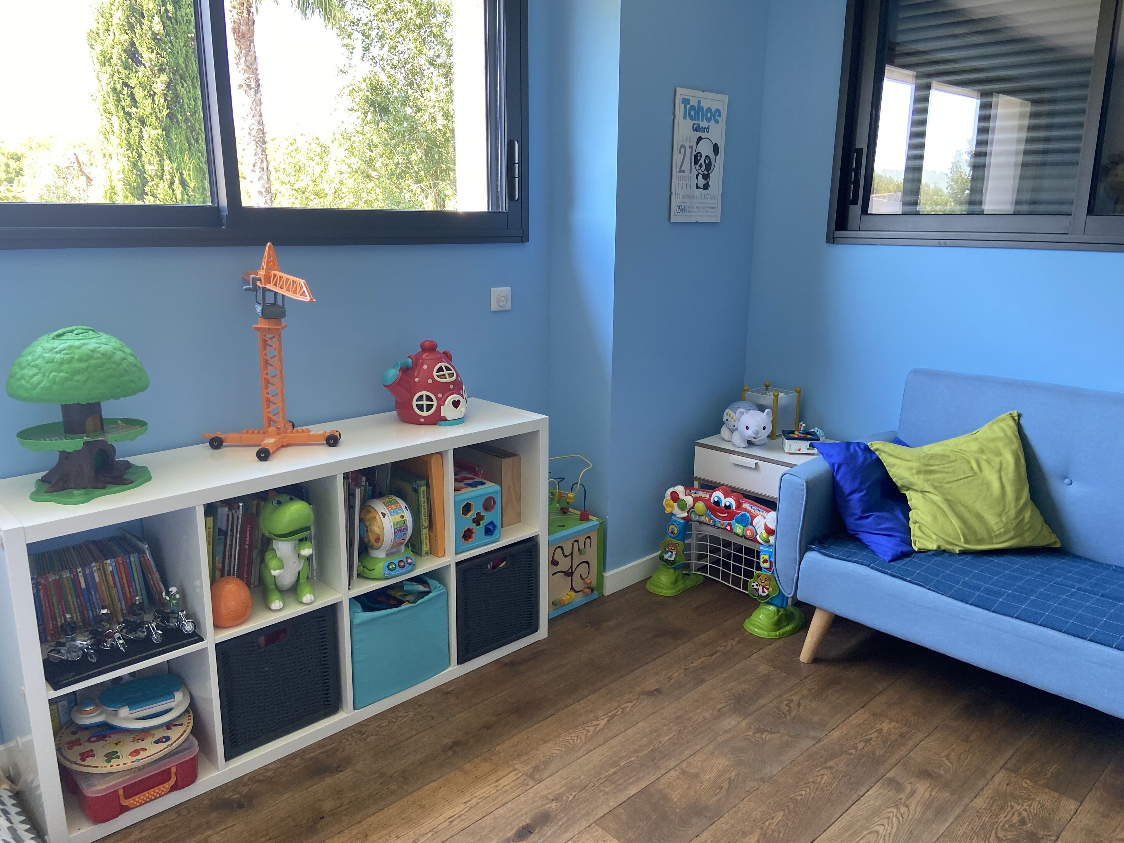A child's playroom with a bookshelf, toys, and a blue sofa.