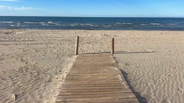 A wooden boardwalk leading to the beach with footprints in the sand.