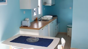 Cocina compacta con zona de comedor, que incluye una mesa blanca con dos sillas, un tapete azul y armarios de madera.
