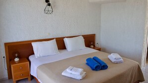 Una cama bien tendida con toallas blancas y azules, una mesita de madera y una lámpara fijada a la pared.