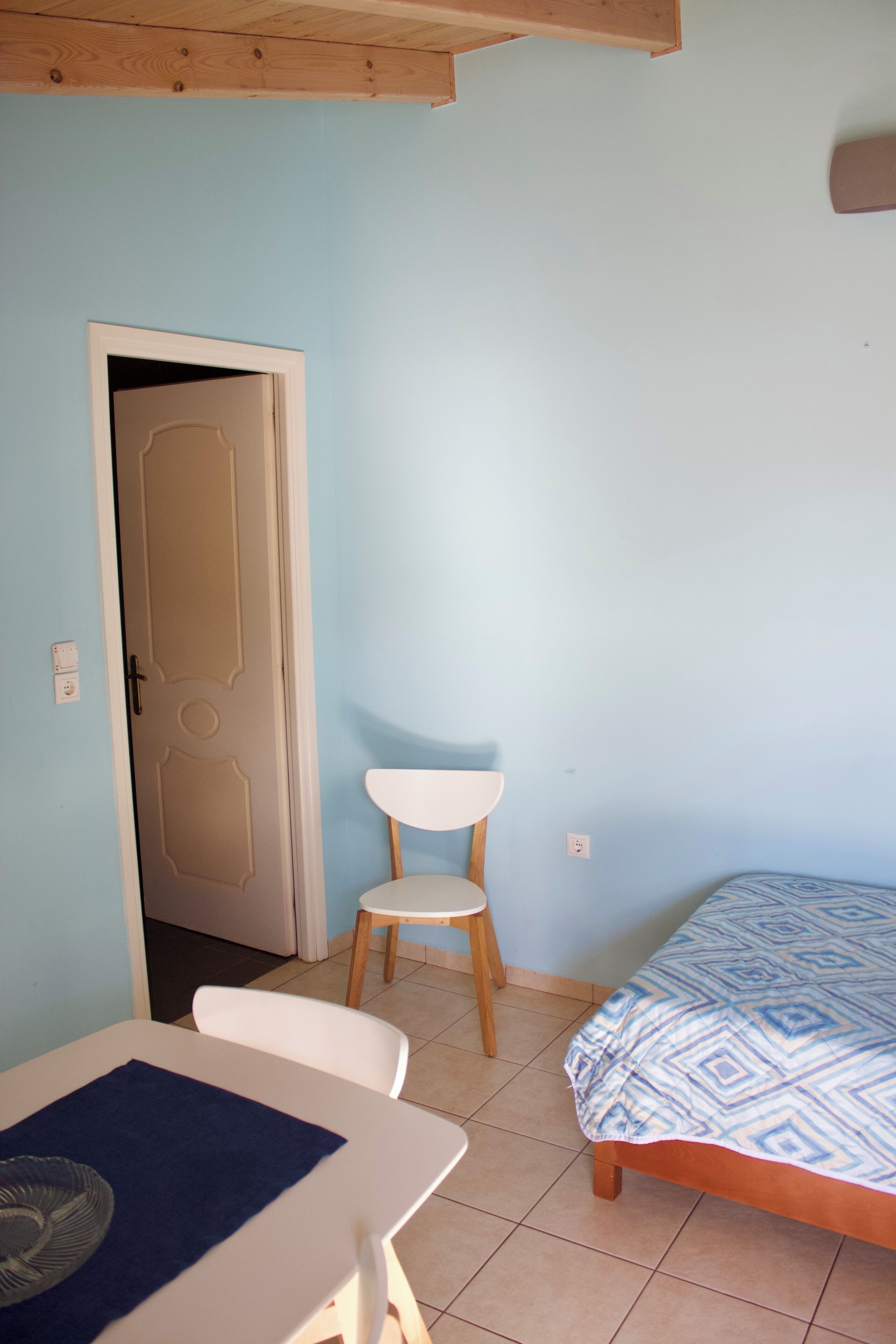 Una habitación con cama, una mesa con sillas, una puerta y un enchufe.