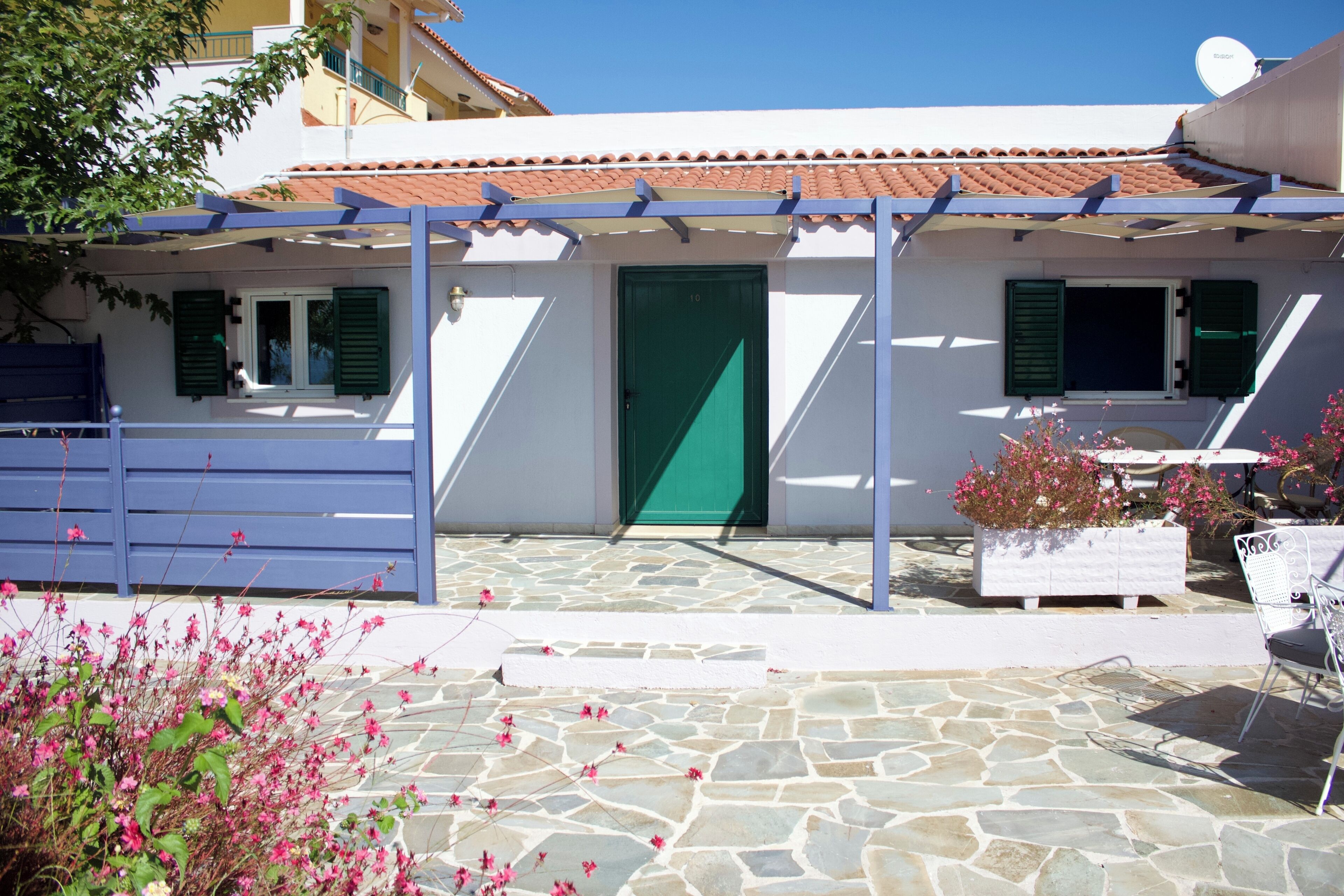 Un bâtiment avec un toit en tuiles, une porte verte et un patio en pierre.