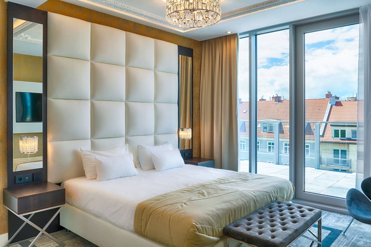 Ein modernes Hotelzimmer mit einem großen Bett, einer Sitzecke, einem großen Fenster mit Stadtblick und einer Chandelüster.