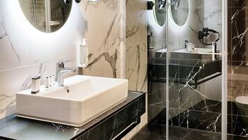 Un baño moderno con tocador de mármol, ducha con mampara de vidrio y dos espejos montados en la pared.