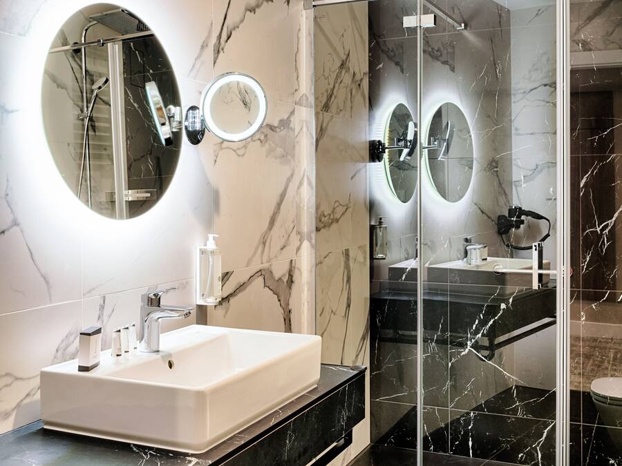 Un baño moderno con tocador de mármol, ducha con mampara de vidrio y dos espejos montados en la pared.