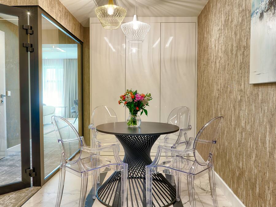 A modern dining area with a round table, clear chairs, and a vase of flowers.