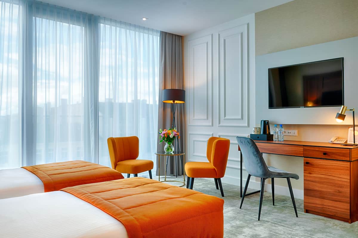Ein Hotelzimmer mit einem Bett, zwei Stühlen, einem Schreibtisch, einem Fernseher und einer Lampe.