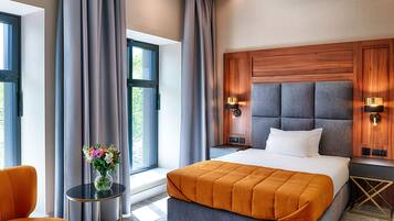 Una habitación de hotel moderna con una cama grande, una mesita de noche con un florero y vistas a la vegetación.