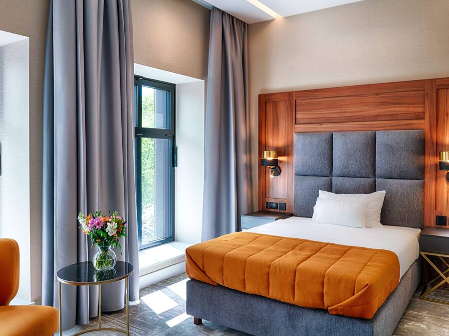 Una habitación de hotel moderna con una cama grande, una mesita de noche con un florero y vistas a la vegetación.