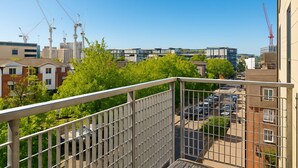 A balcony with a metal railing overlooking a parking lot and buildings.