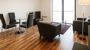 A modern living room with a glass table, black chairs, a grey sofa, and a floor lamp.