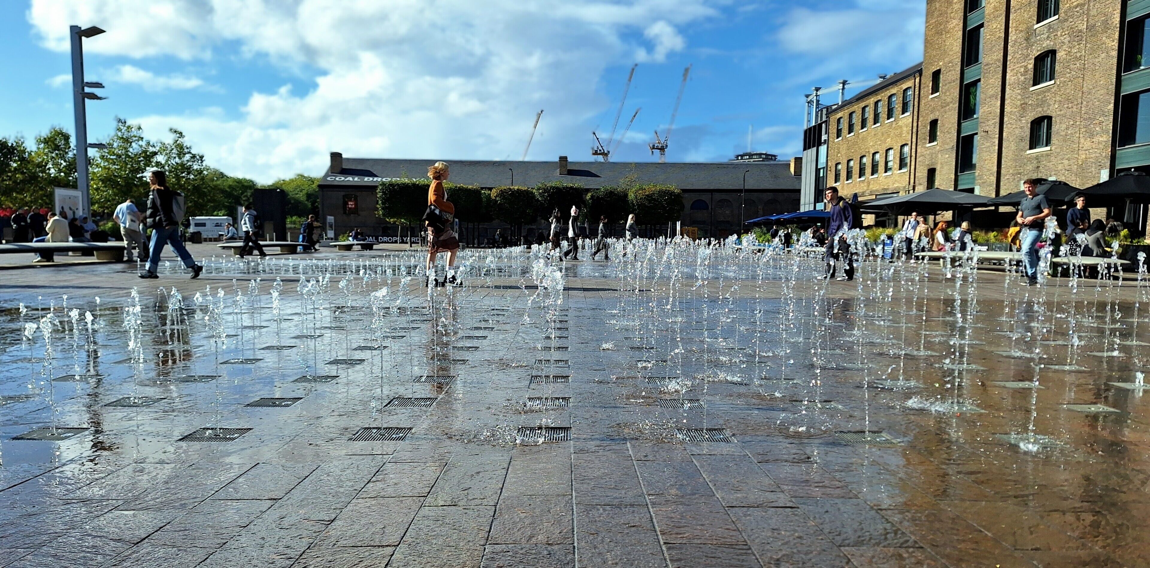 A public square with a water feature and people walking around.