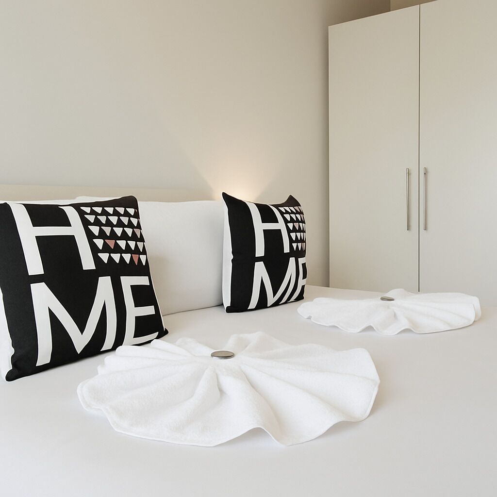 Une pièce au décor minimaliste, avec un canapé blanc, deux coussins noirs et blancs, et une serviette blanche posée sur le sol.