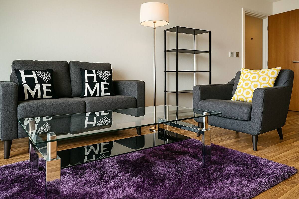 A modern living room with a grey sofa, a matching armchair, a glass coffee table, and a purple rug.